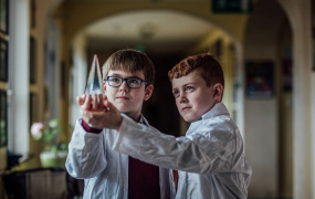 Two boys in science coats holding and looking at a beaker