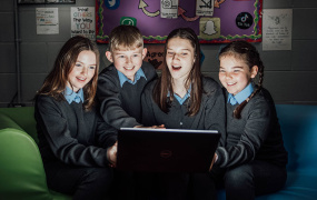 School children looking at an open laptop with surprised expressions.
