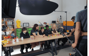 5 people in a row making spool racers being filmed by a camera crew