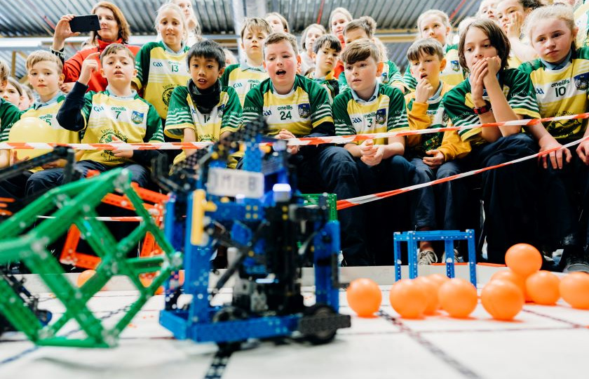 Crowd of children in green and gold watching their robot