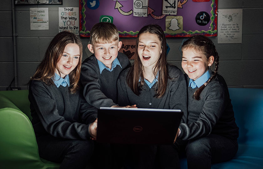 Three female and one male student looking excited and surprised at laptop screen