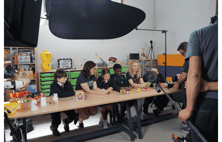 5 people in a row making spool racers being filmed by a camera crew